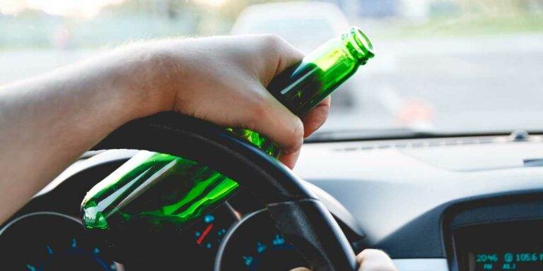 Picture of a person driving while holding an open beer bottle